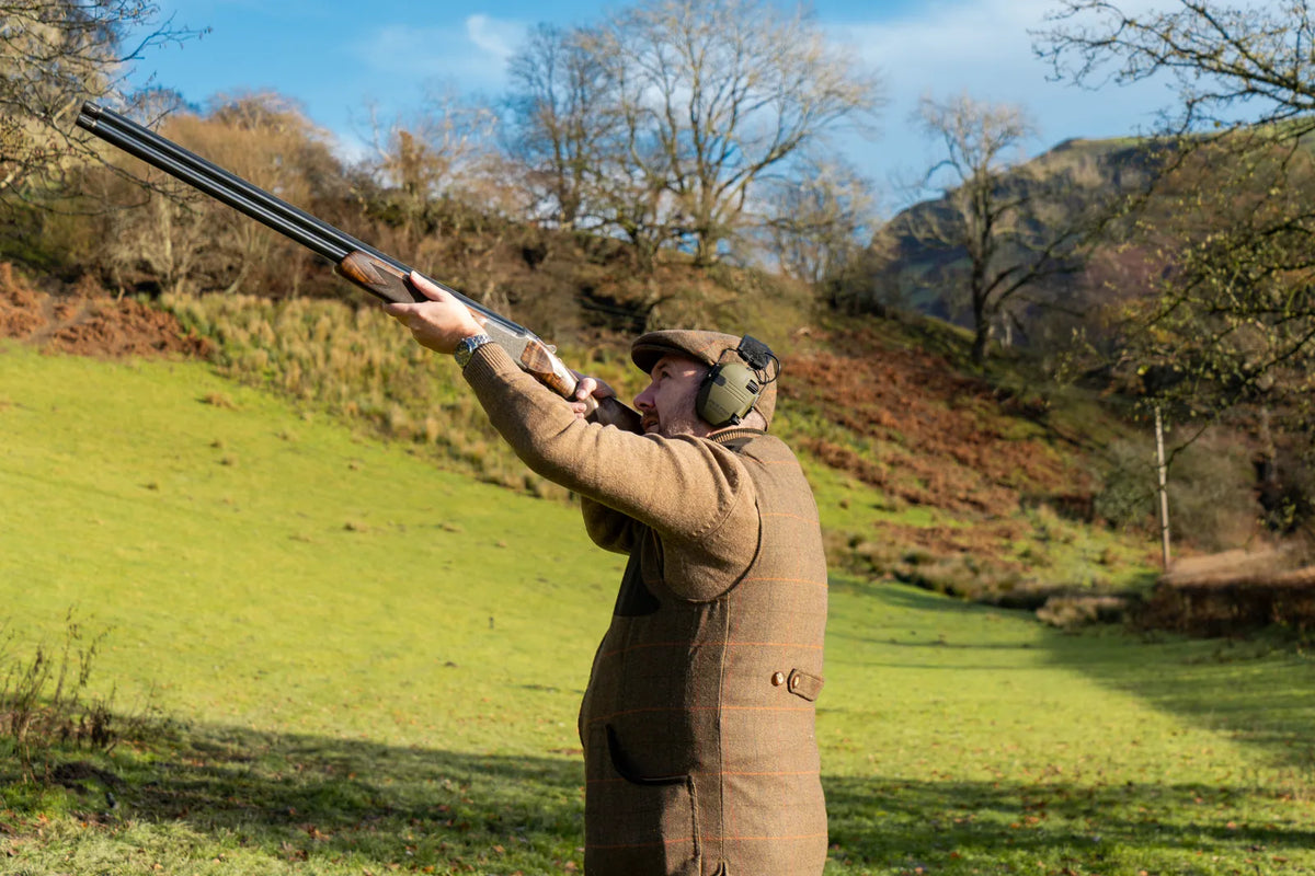 Shooter in a tweed waistcoat and cap taking a shot on country ground