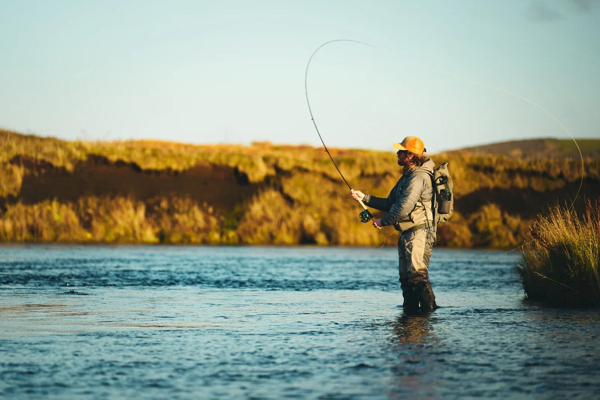 Angler wearing waders and a layered fishing outfit while casting on a river