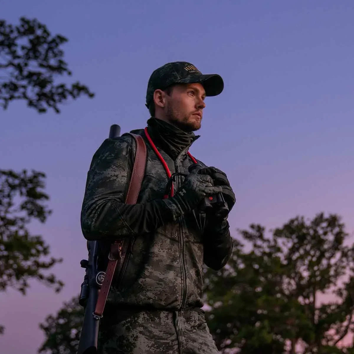 Shooter in a dark field jacket at dusk with a gun over one shoulder
