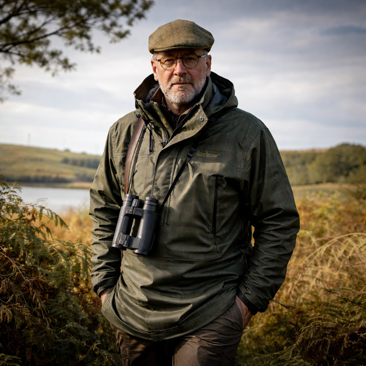 Man wearing a Deerhunter Pro Gamekeeper Smock with binoculars standing in a natural landscape